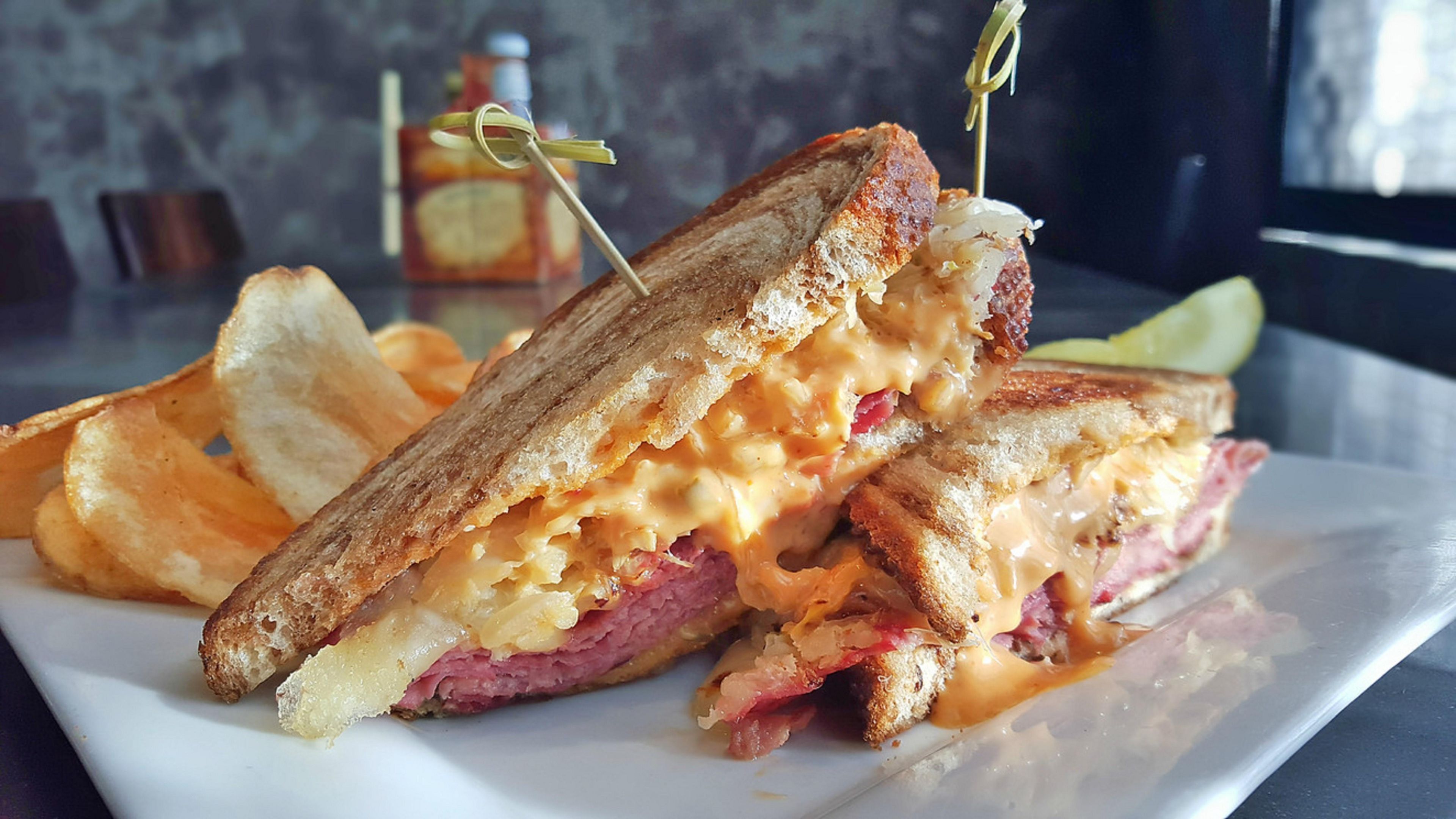 A grilled sandwich with melted cheese and a toothpick, served on a white plate with potato chips.