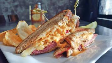 A grilled sandwich with melted cheese and a toothpick, served on a white plate with potato chips.