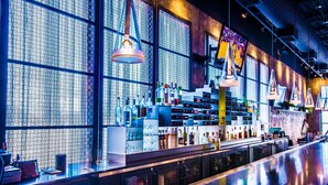 A modern bar with a patterned wall, shelves of bottles, and hanging pendant lights.