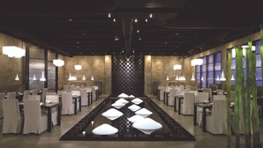 A restaurant with a long dining table, multiple chairs, and hanging lights.