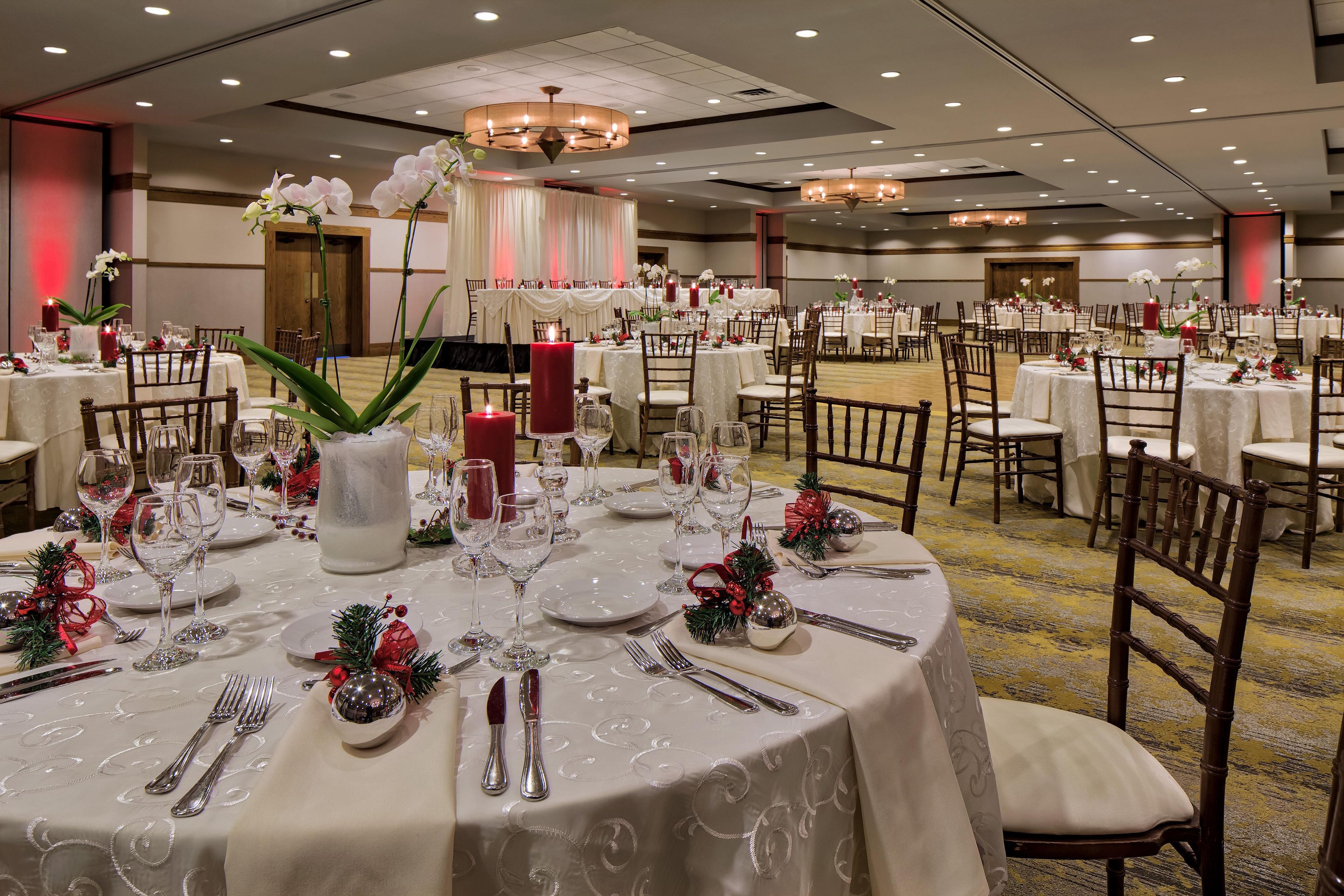 Un salón de banquetes con mesas redondas dispuestas para cenar, con manteles blancos, velas y centros de mesa florales.
