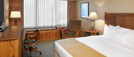 A hotel room with a bed, a desk, a chair, a television, and a window with curtains.