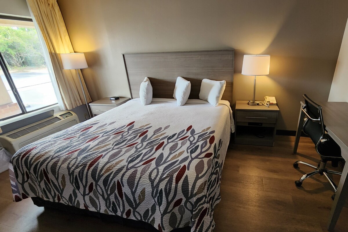 Quarto de hotel com uma cama grande, duas mesas de cabeceira, uma escrivaninha e uma cadeira.