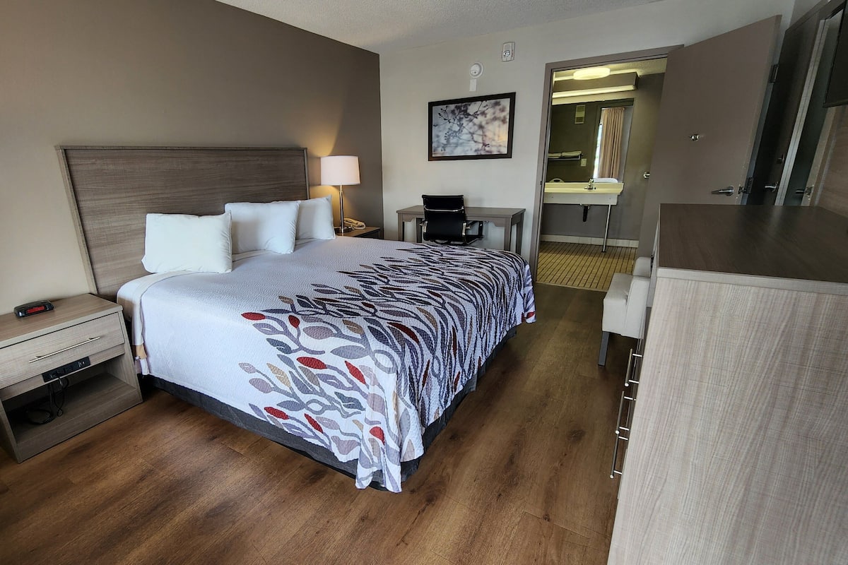 A hotel room with a bed, bedside table, lamp, and a desk with a chair.