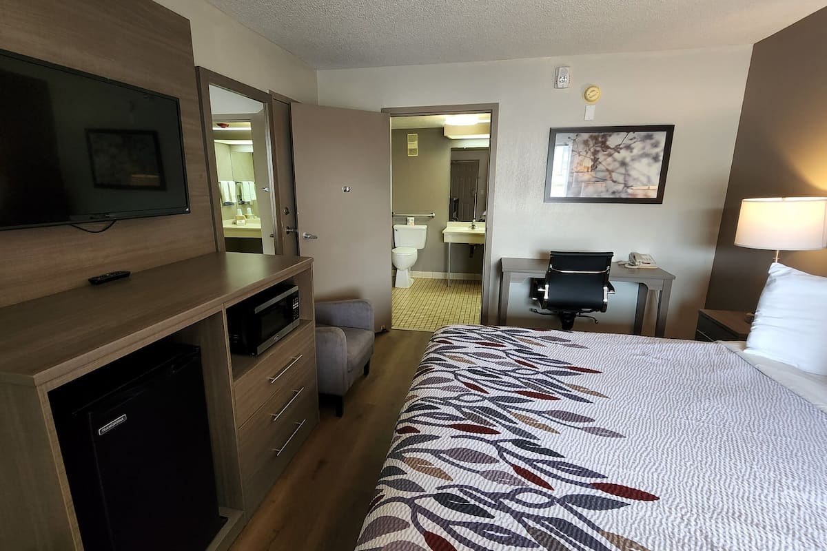 A hotel room with a bed, a desk, a chair, a television, and a small refrigerator.