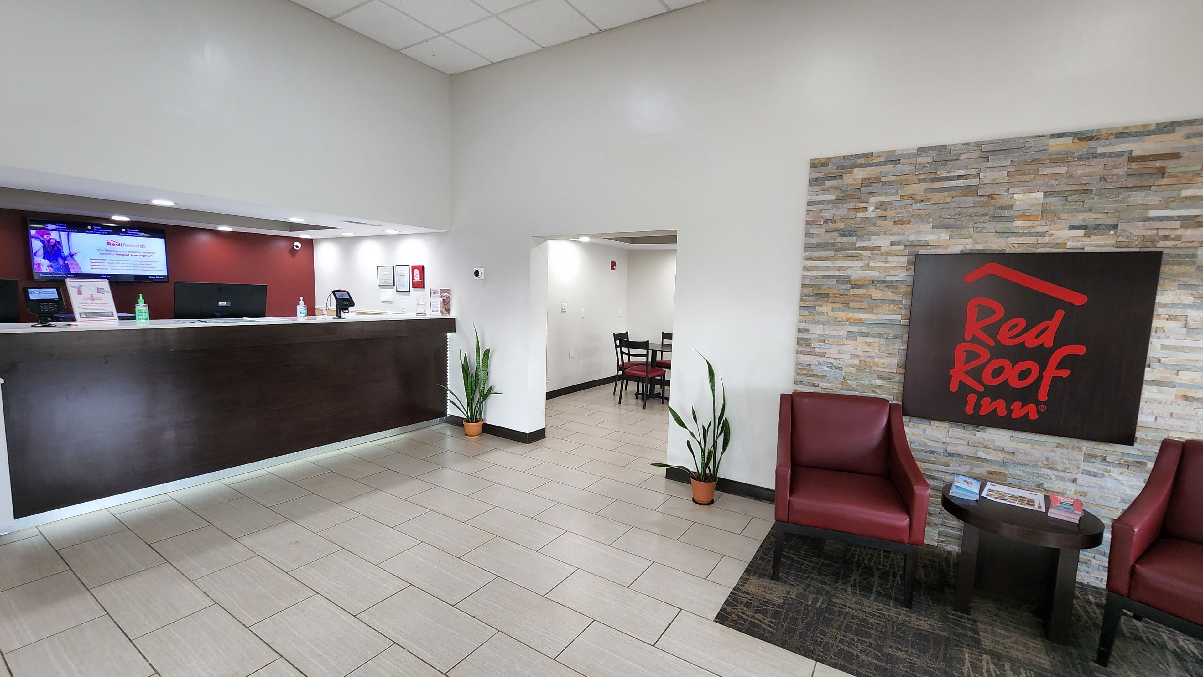 A reception area with a counter, a Red Roof Inn sign, a seating area with chairs, and a dining table.