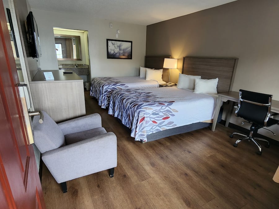Habitación de hotel con cama, dos mesitas de noche, un escritorio con silla, televisor y baño visible a través de una puerta abierta.