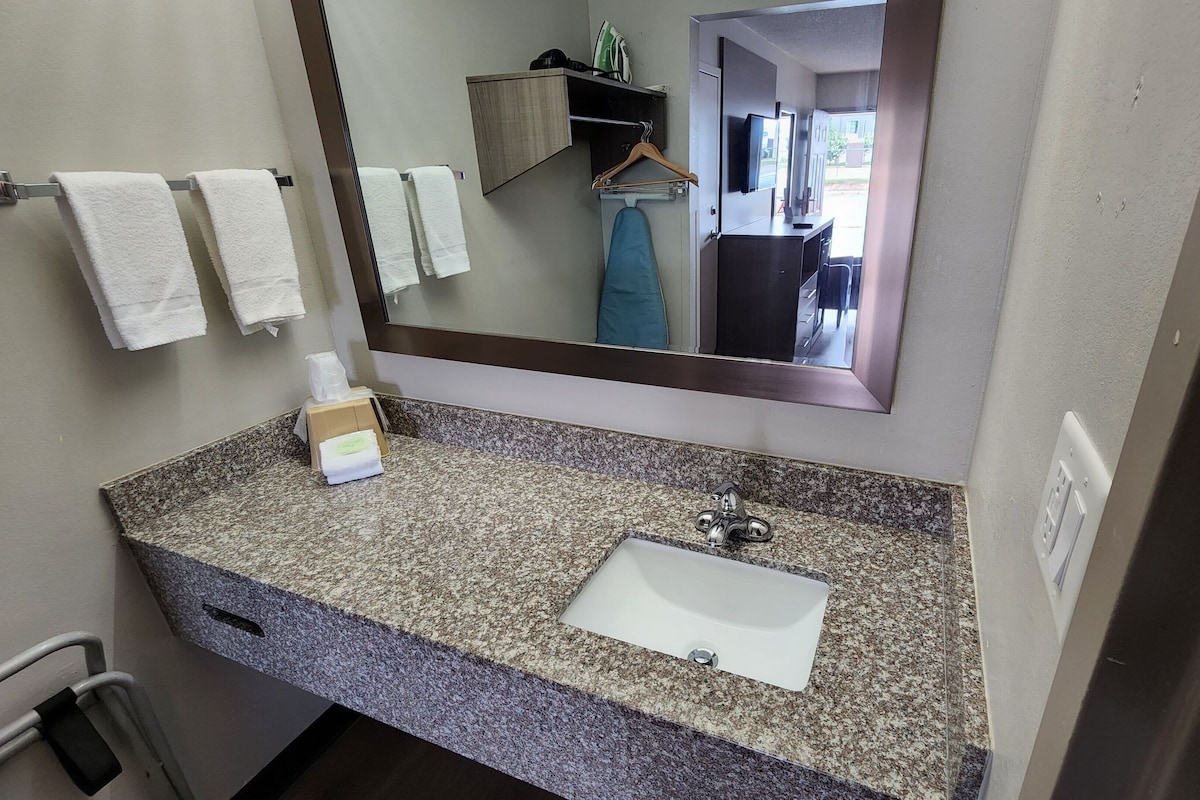 A bathroom with a granite countertop, a white sink, a mirror, and a towel rack with three towels.