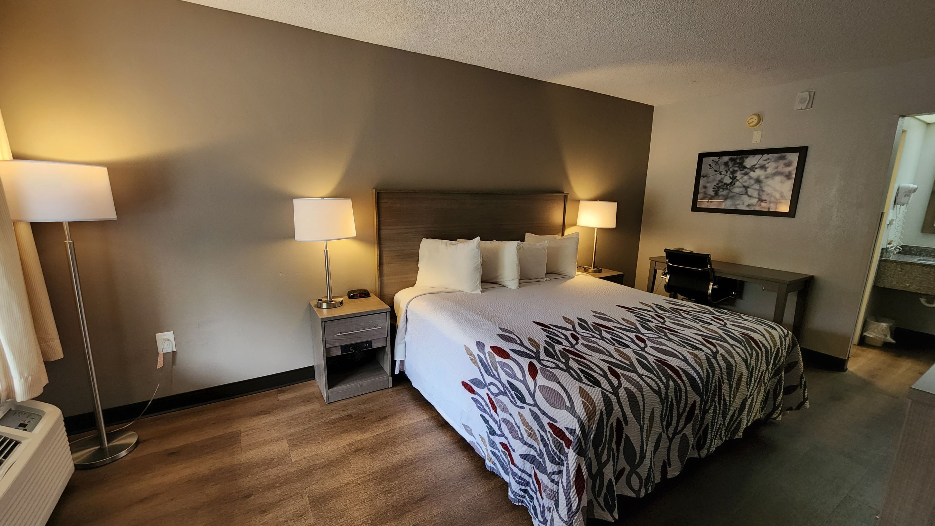 A hotel room with a large bed, two bedside tables, a desk, and a chair.