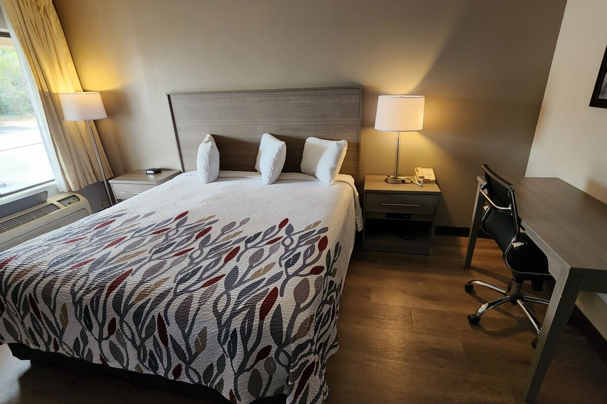 A hotel room with a large bed, two bedside tables, a desk, and a chair.