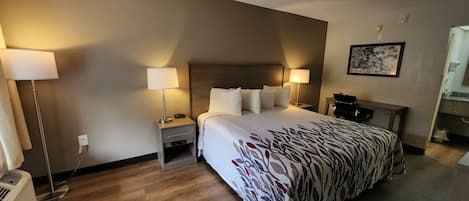 Habitación de hotel con una cama grande, dos mesitas de noche con lámparas, un escritorio con silla y una kitchenette pequeña.