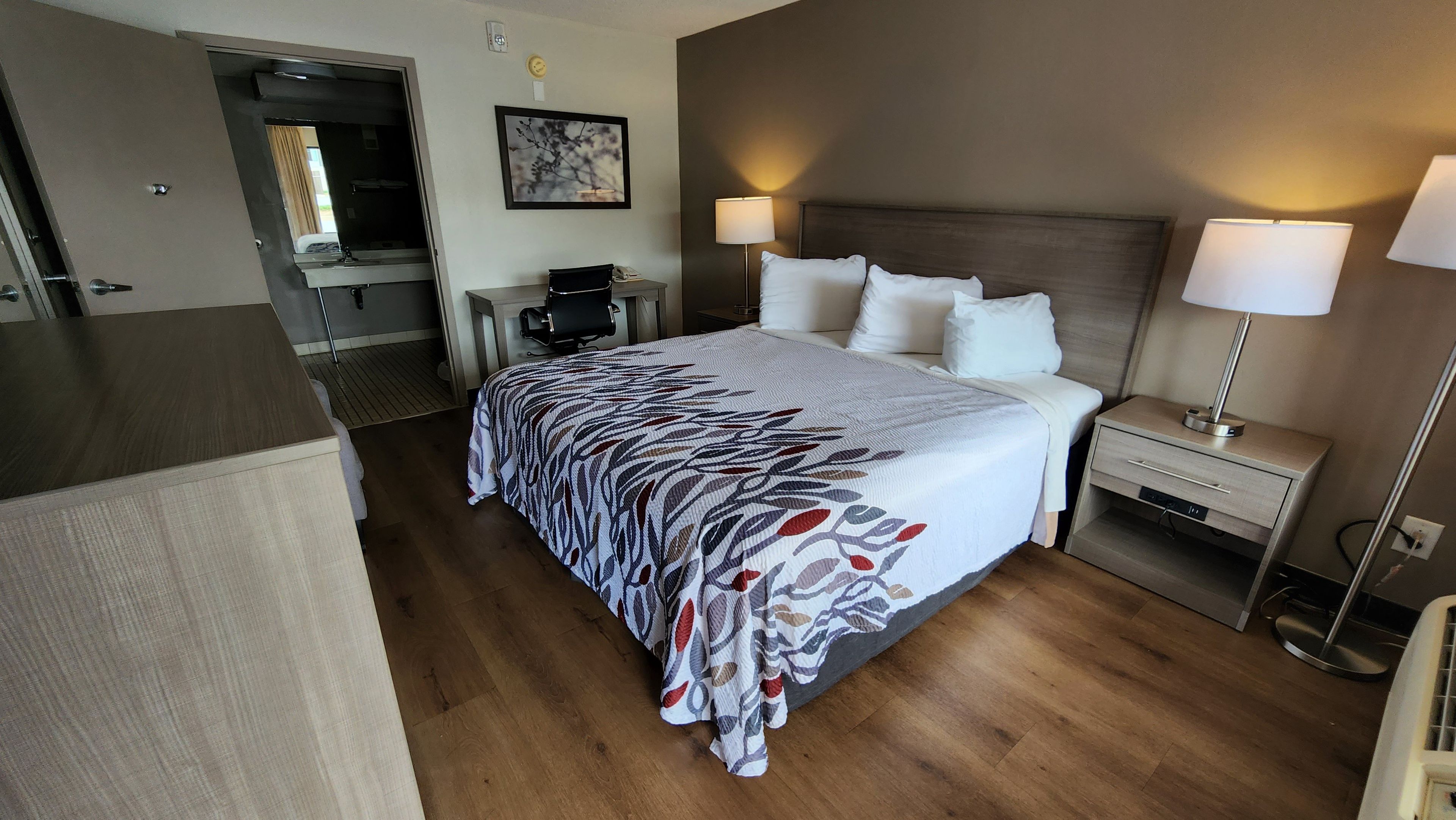Une chambre d’hôtel avec un lit, des lampes de chevet, un bureau et une chaise.