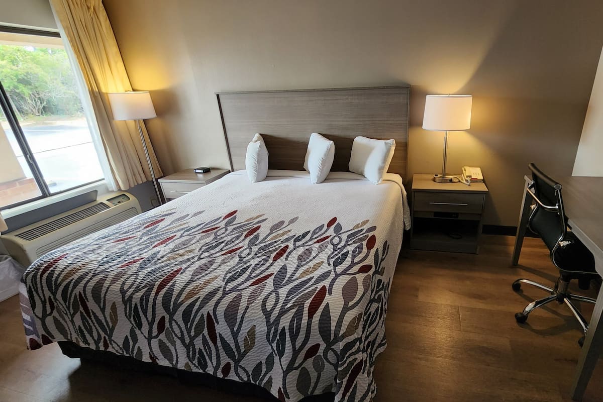 Quarto de hotel com uma cama grande, duas mesas de cabeceira, uma escrivaninha e uma cadeira.