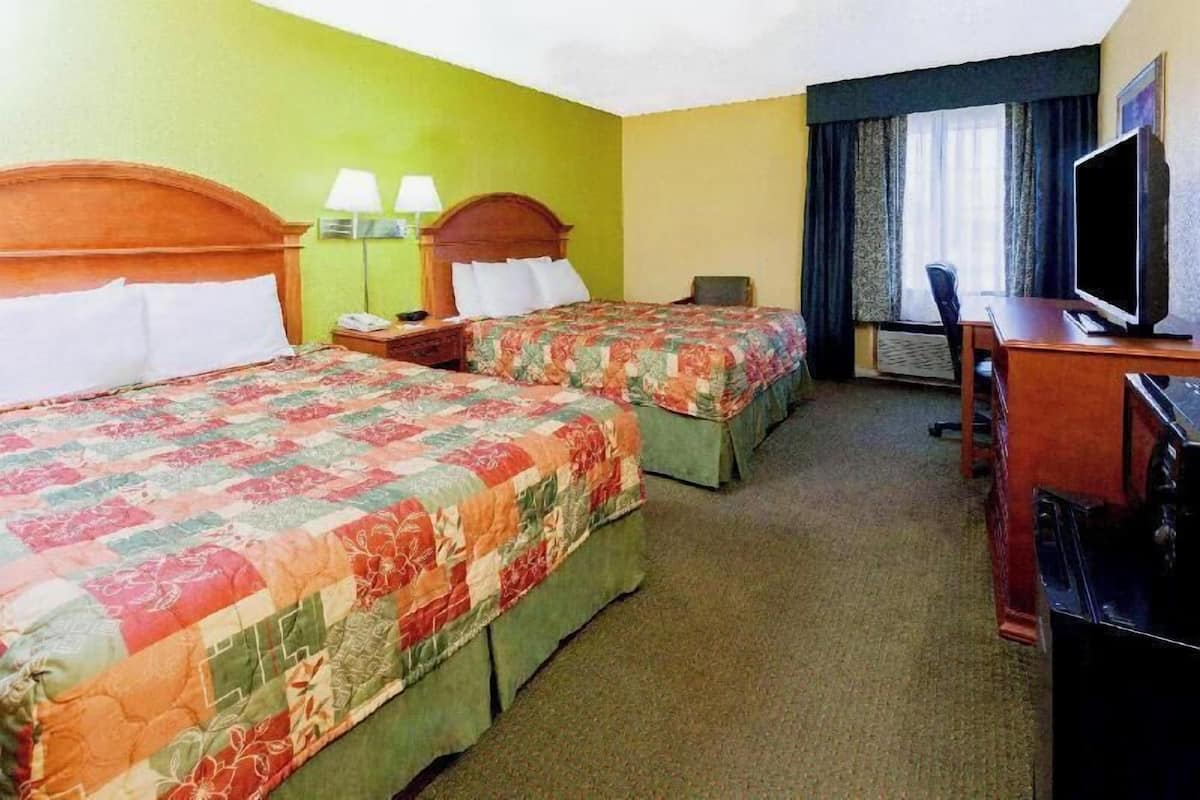 A hotel room with two beds, a desk, a chair, a TV, and a window with curtains.