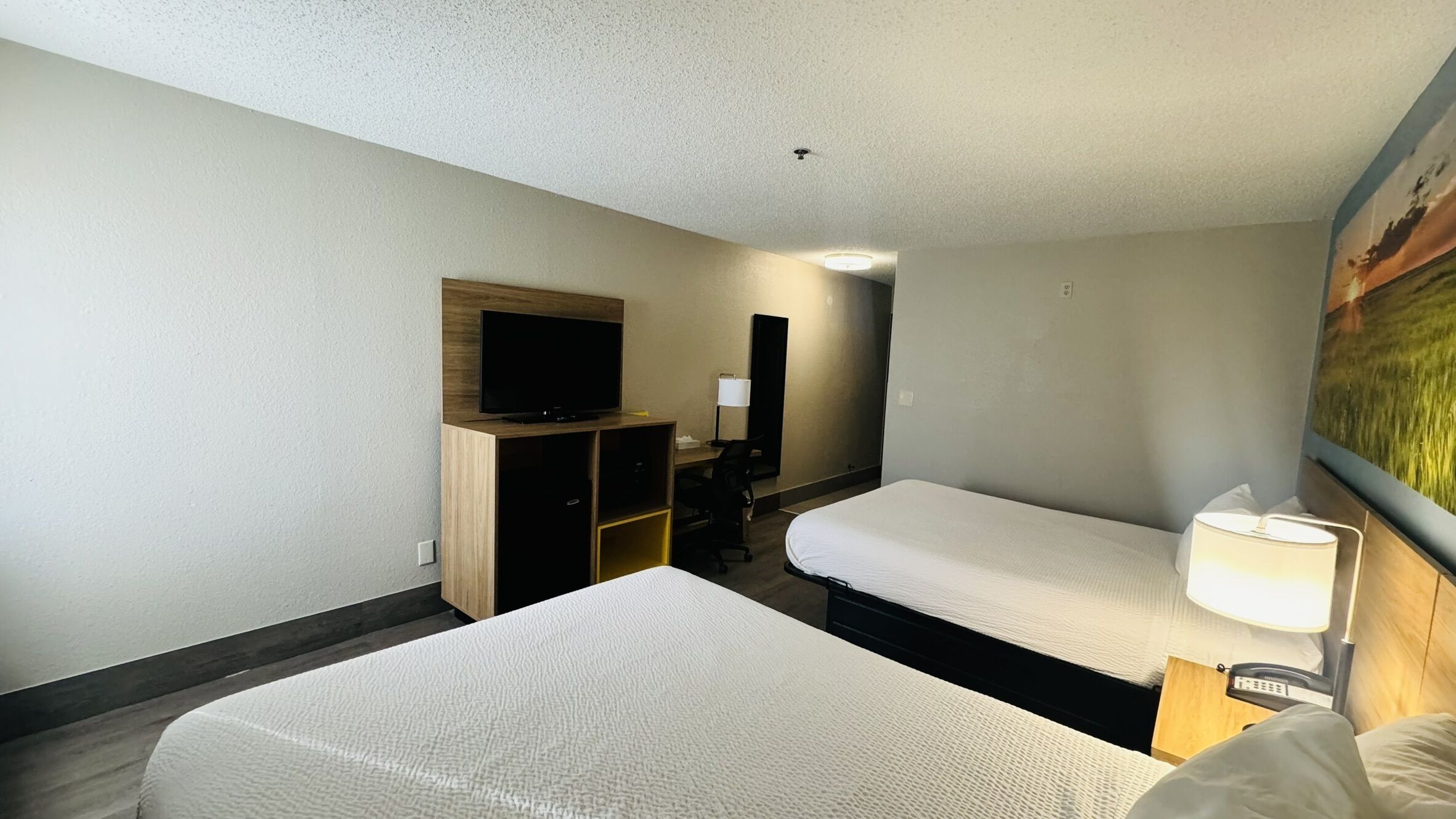 A hotel room with two single beds, a TV on a wooden cabinet, a desk with a chair, and a painting on the wall.