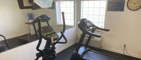 A fitness center with exercise equipment, a clock, and a safety rules sign.