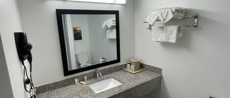 Un baño moderno con encimera de granito, un lavamanos, un espejo, un perchero para toallas y un dispensador de papel higiénico.