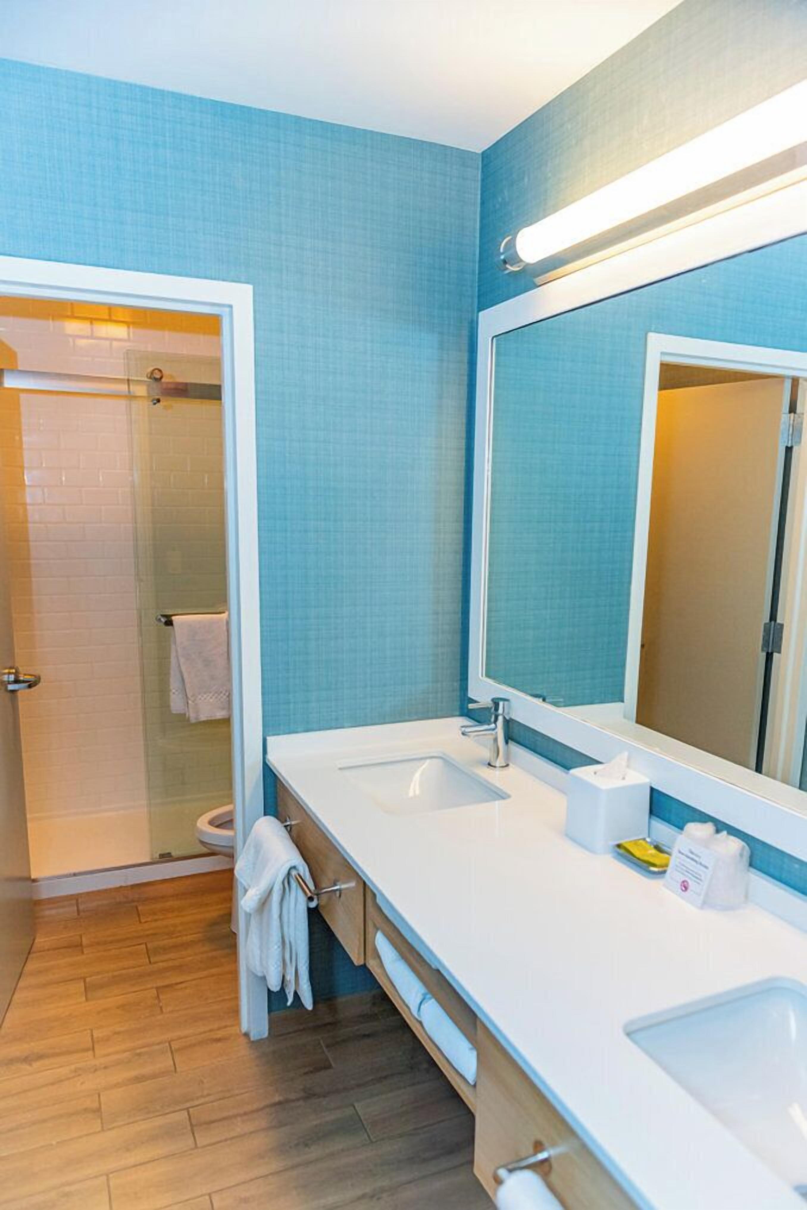 Une salle de bain moderne avec un grand miroir, deux lavabos et une douche.