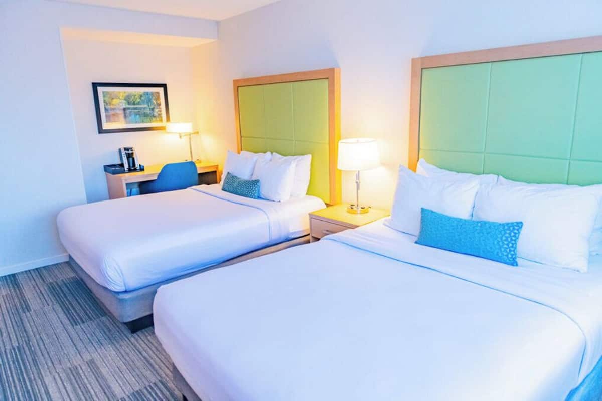 A hotel room with two beds, a desk, and a chair.