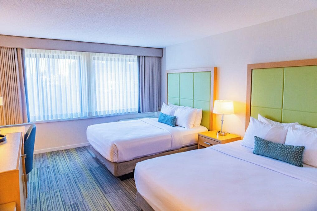 A hotel room with two beds, a desk, and a chair.