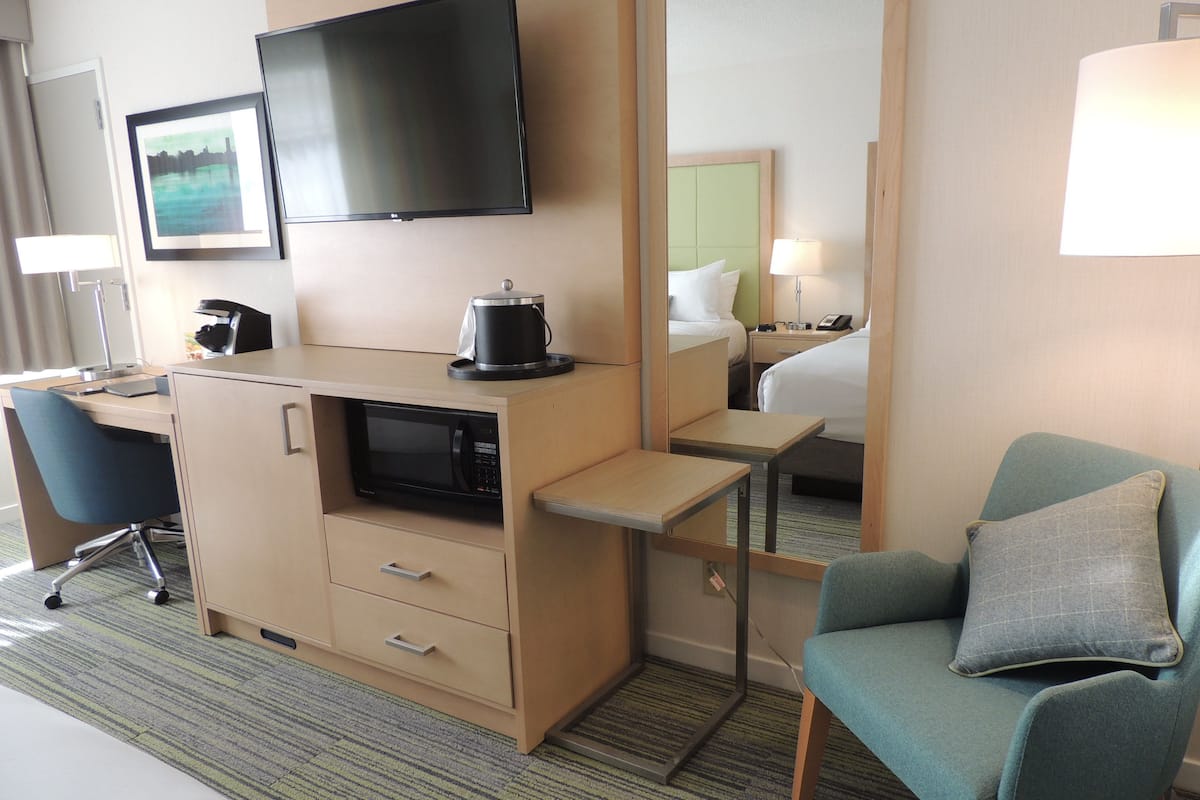 A hotel room with a bed, a desk with a computer, a chair, a television, and a coffee maker.