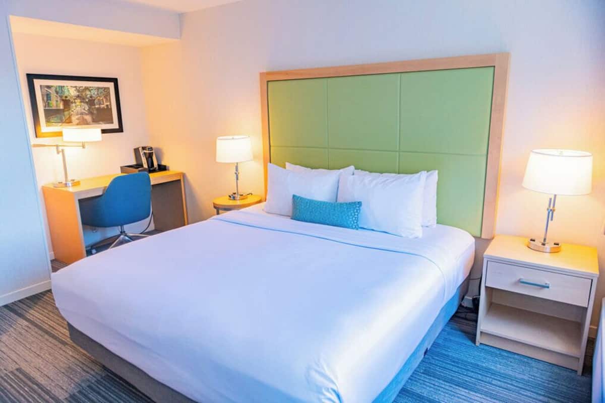 A hotel room with a large bed, two bedside tables with lamps, a desk with a chair, and a framed picture on the wall.