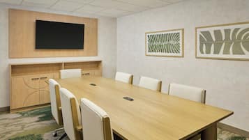 A conference room with a long table, white chairs, a mounted TV, and framed artwork on the walls.