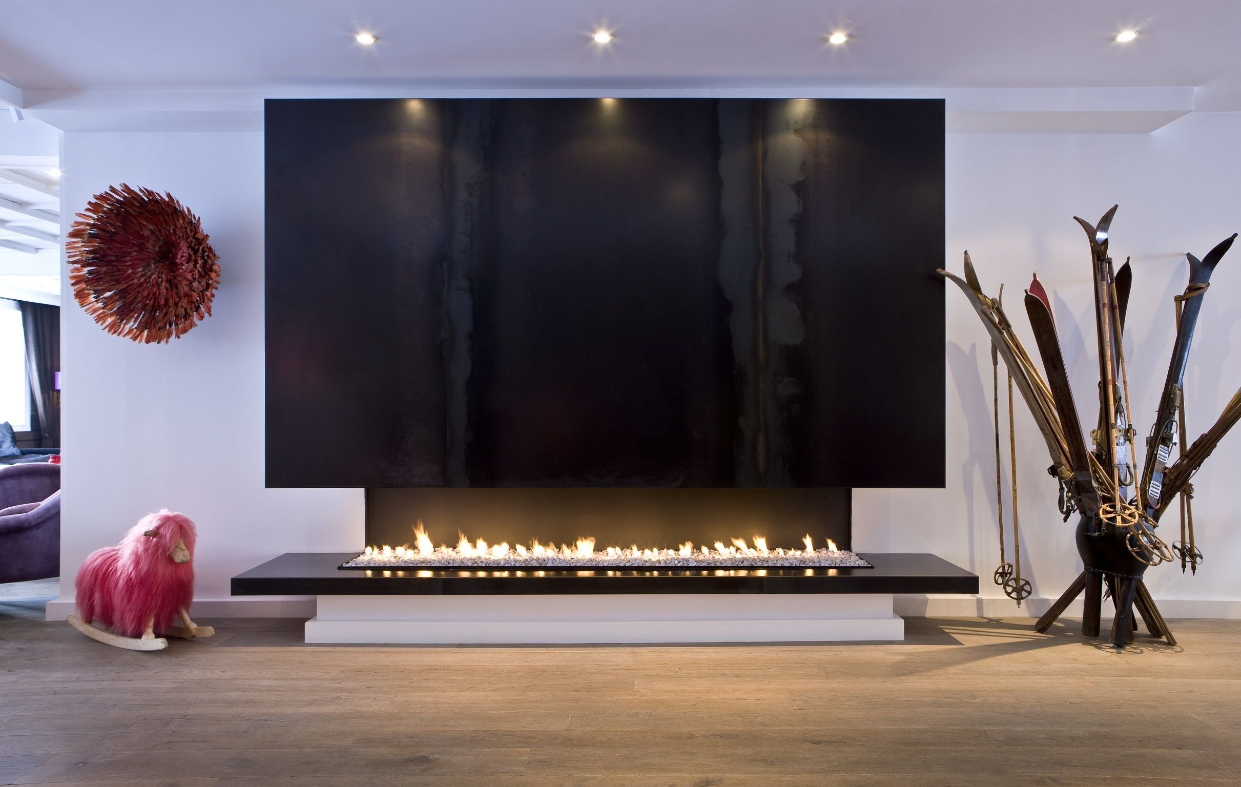 A modern living room with a large flat-screen TV mounted on the wall, a fireplace with a fire, and a decorative plant arrangement.