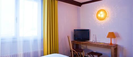 Habitación de hotel con dos camas, un escritorio con televisor, una silla, una lámpara y un accesorio de luz en la pared.