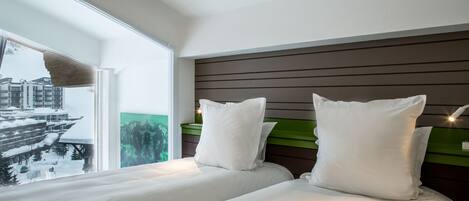 A hotel room with a bed, pillows, a headboard, and a window with a view of a snowy landscape.