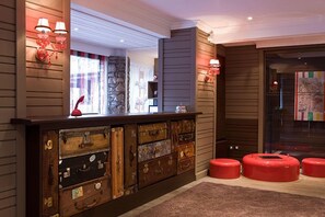A reception area with a wooden counter, vintage suitcases, and red stools. - Hotel Ormelune (Val-d'Isere)