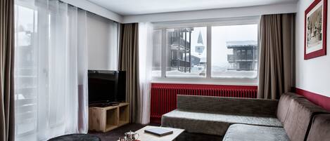 A modern hotel room with a sofa, a television, a coffee table, and a view of a snowy landscape through the window.