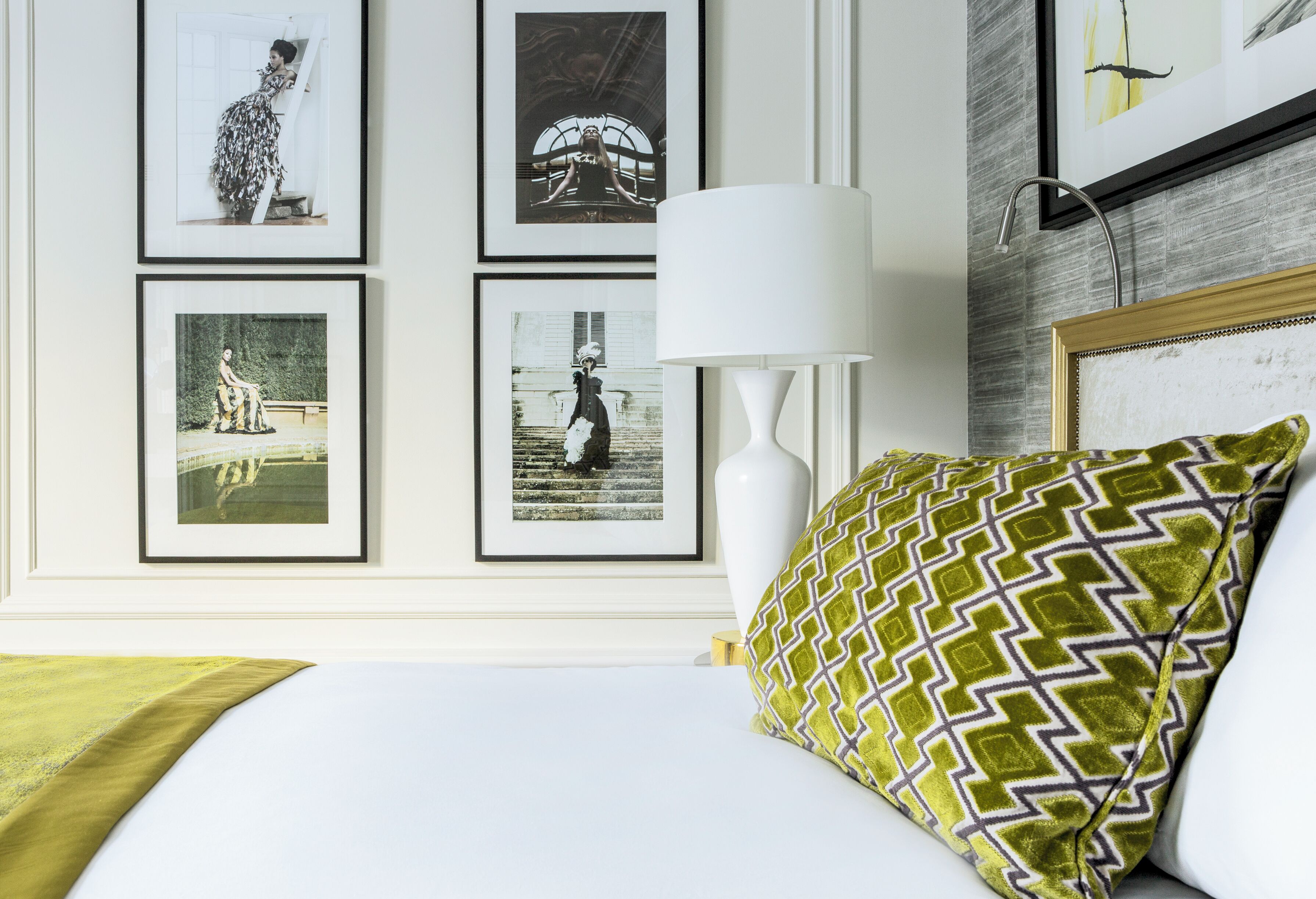 A neatly arranged hotel room with a bed, a white lamp, and framed photographs on the wall.