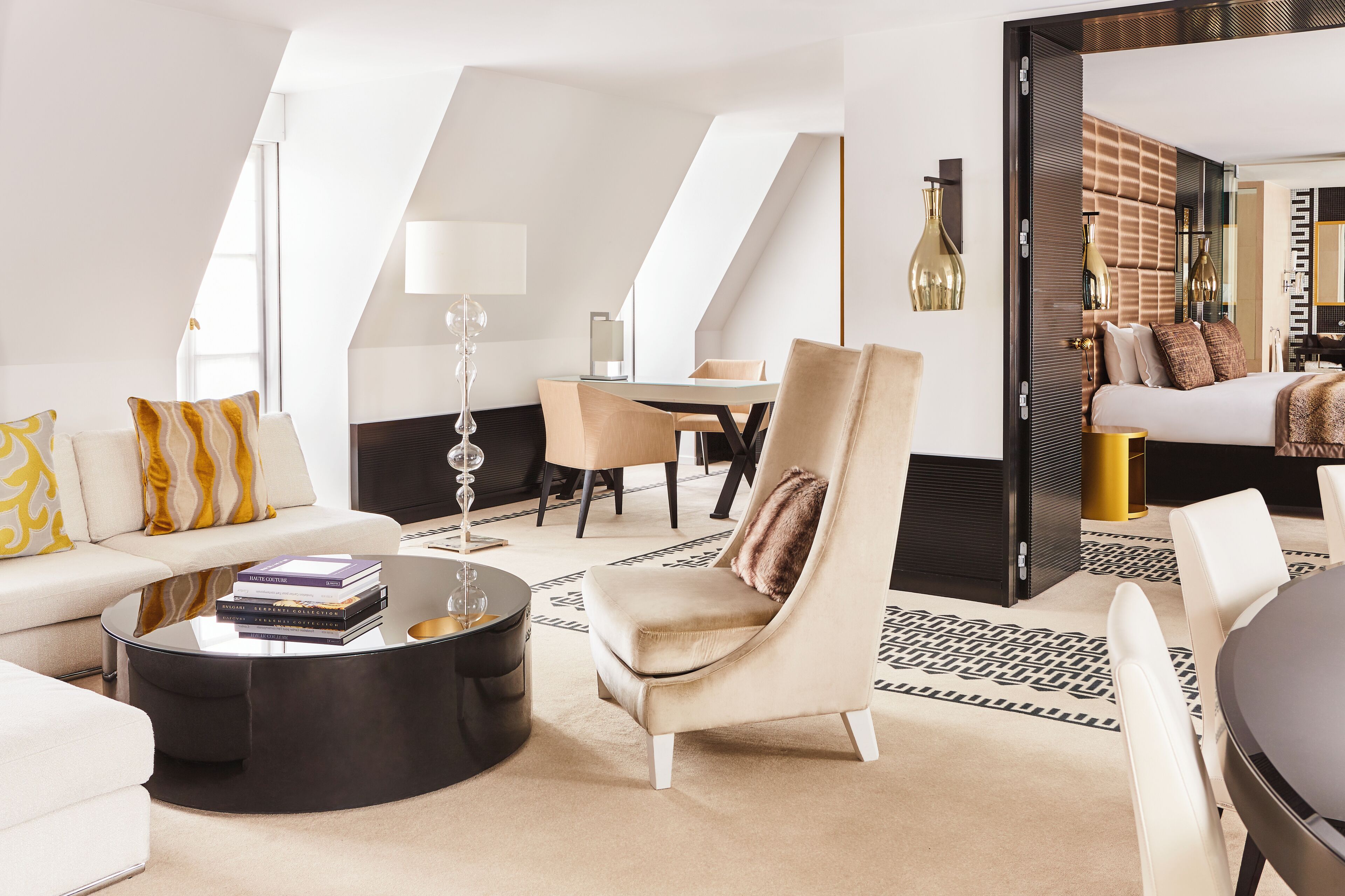 A modern hotel room with a loft-style ceiling, a sofa set, a round coffee table, and a bed with a headboard.