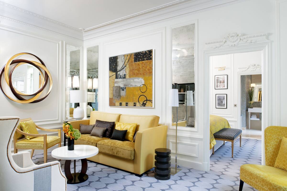 A room with a yellow sofa, a round mirror, and a painting on the wall.