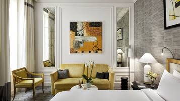 A hotel room with a yellow sofa, a bed, a coffee table, a lamp, and a painting on the wall.