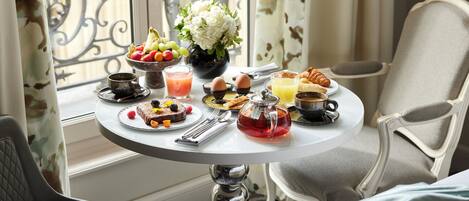 A breakfast table with a variety of food items, a vase of flowers, and a view of the outdoors.