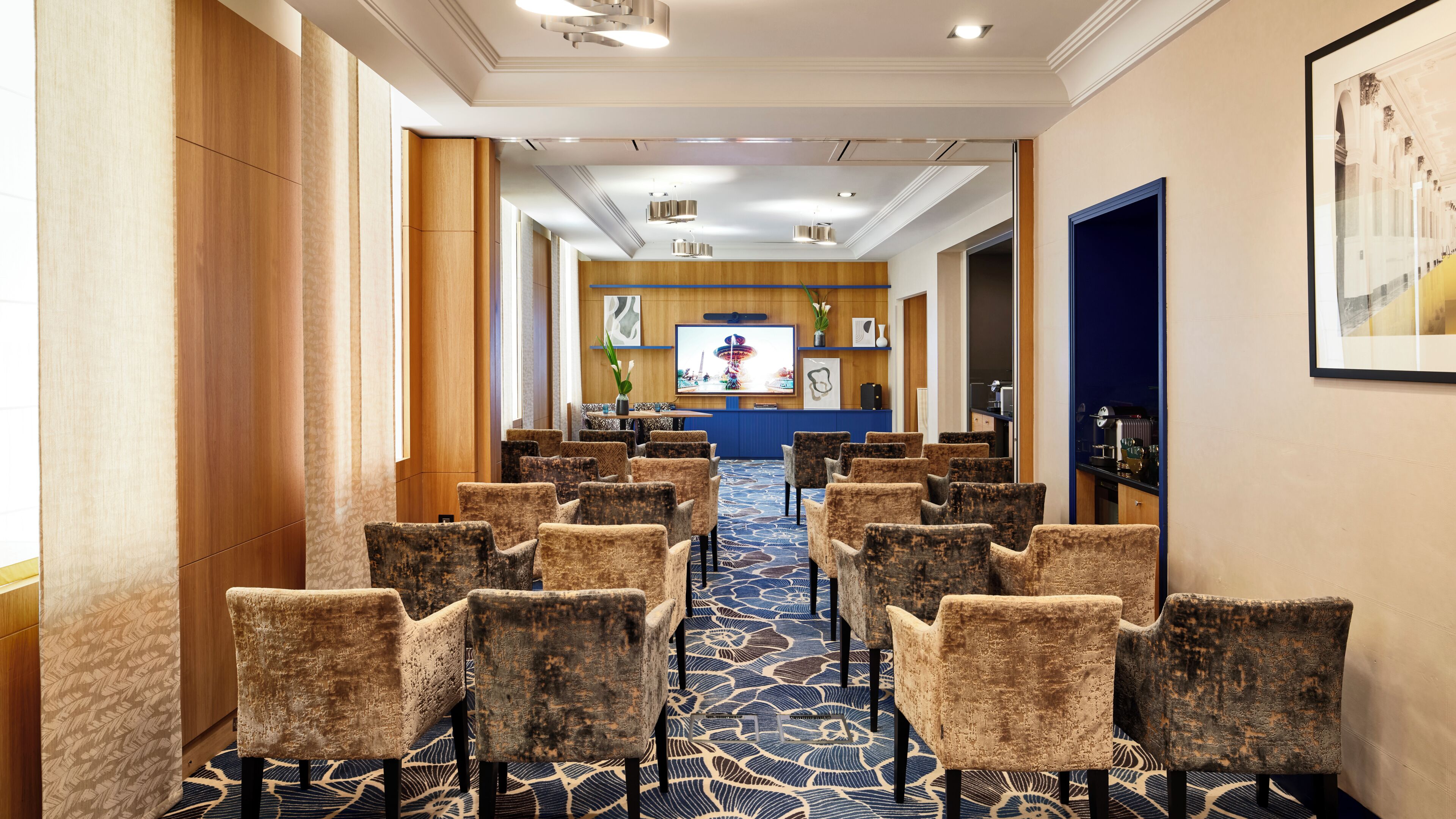 A hotel lobby with a long row of chairs, a reception desk, and a television screen.