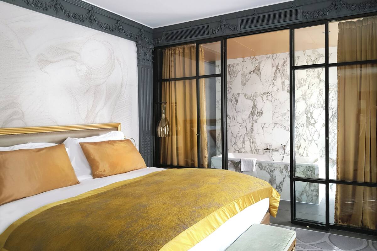 A bedroom with a large bed, a view of a balcony, and a marble wall.