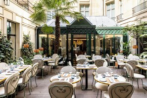 An outdoor dining area with tables and chairs, a palm tree, and a building in the background. - Sofitel Paris Le Faubourg (Paris)