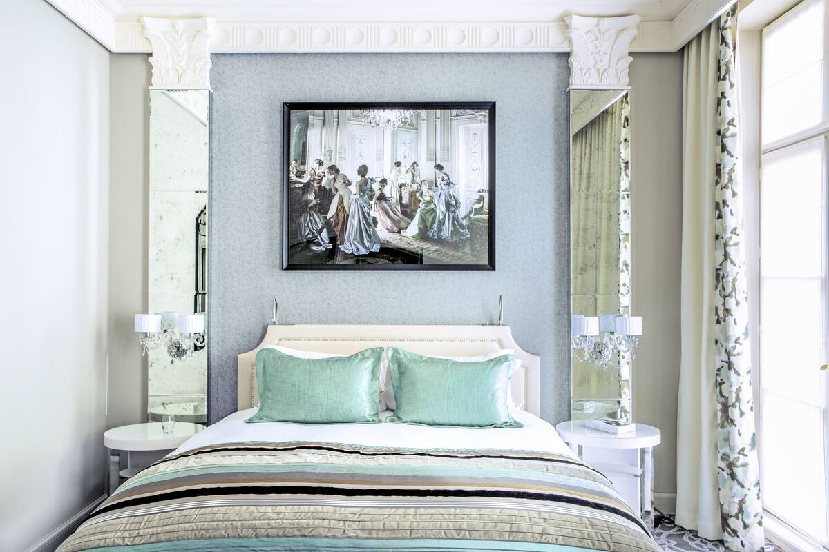 A bedroom with a large bed, two bedside tables, a mirror, and a framed painting on the wall.