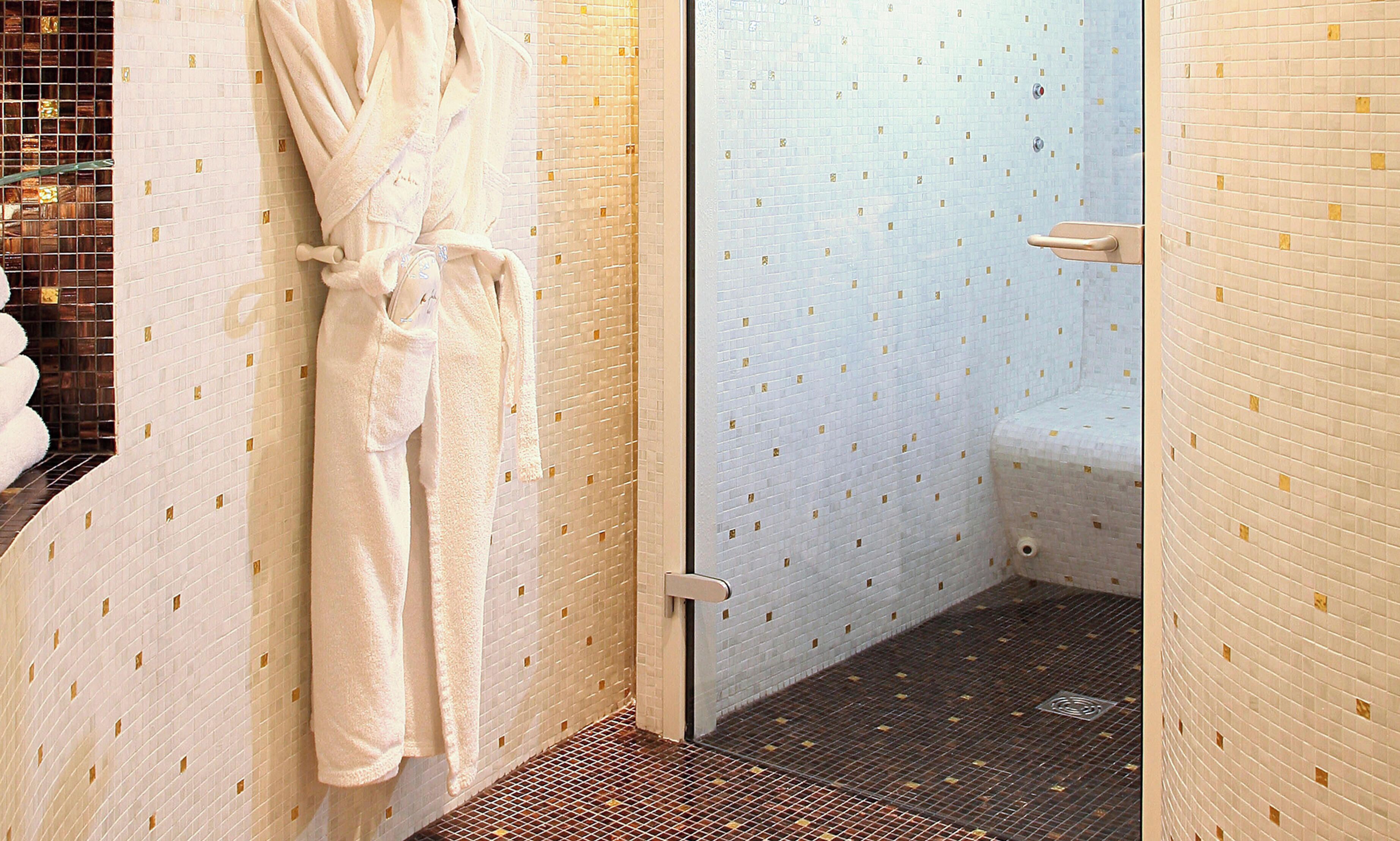 A bathroom with a white bathtub, a glass shower enclosure, and a white bathrobe hanging on the wall.