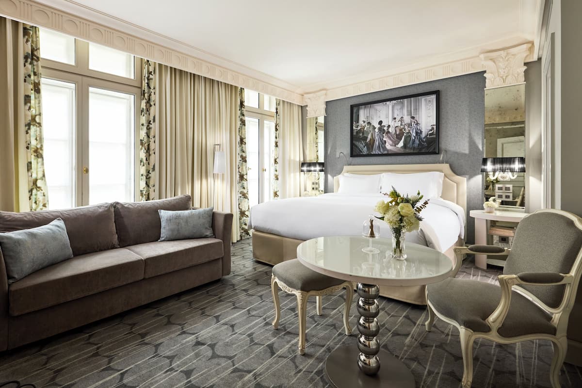 A hotel room with a large bed, a sofa, a round table, and a chair.