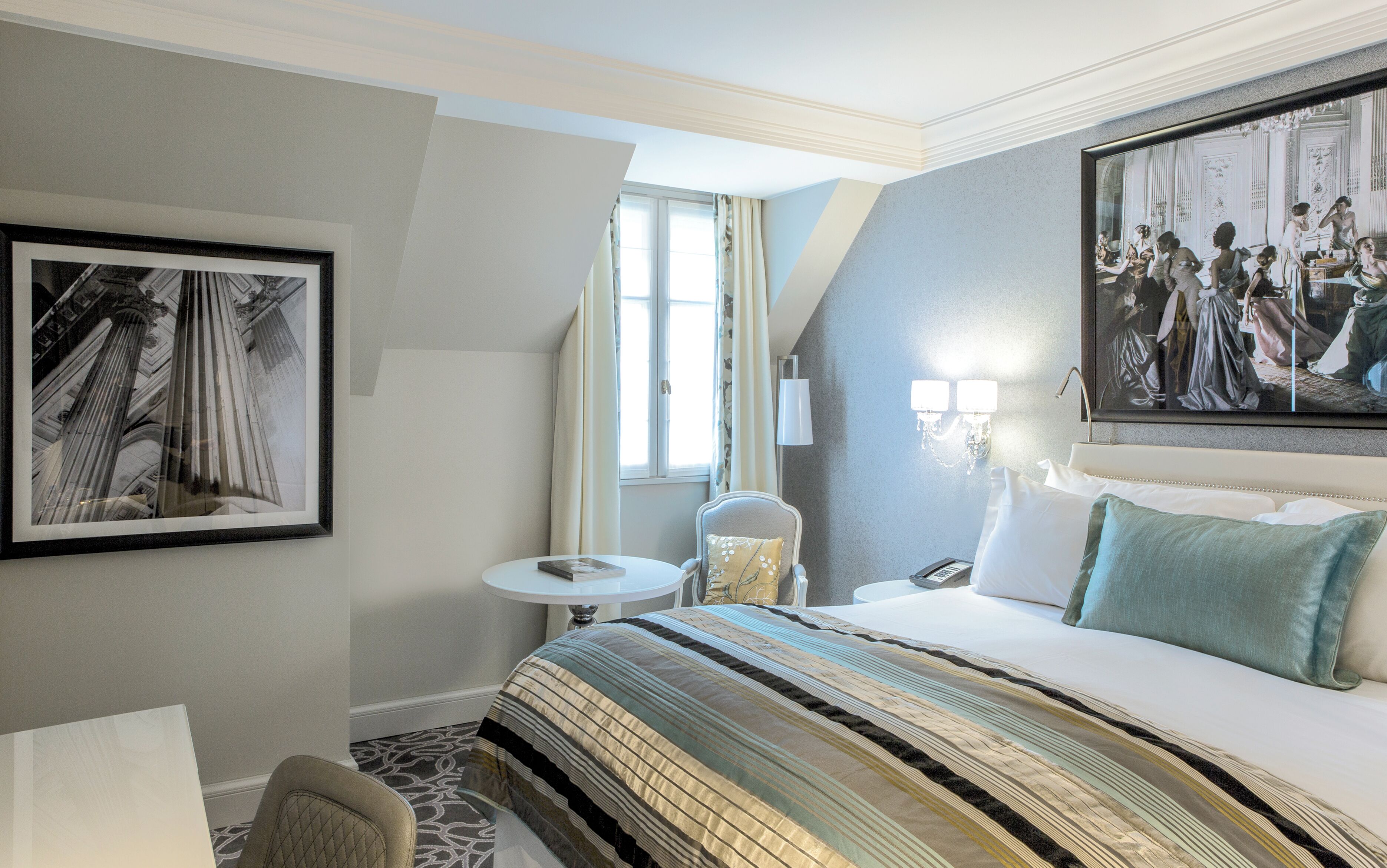 A hotel room with a large bed, a small round table, a chair, and a framed picture on the wall.