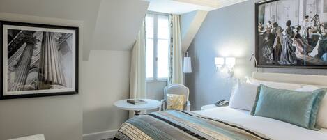 A hotel room with a large bed, a small round table, a chair, and a framed picture on the wall.