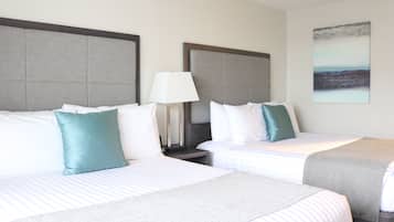 Une chambre d’hôtel avec deux lits, chacun doté d’une tête de lit grise, de draps blancs et d’un oreiller turquoise. Une lampe se trouve sur la table de chevet entre les lits, et un tableau est accroché au mur.