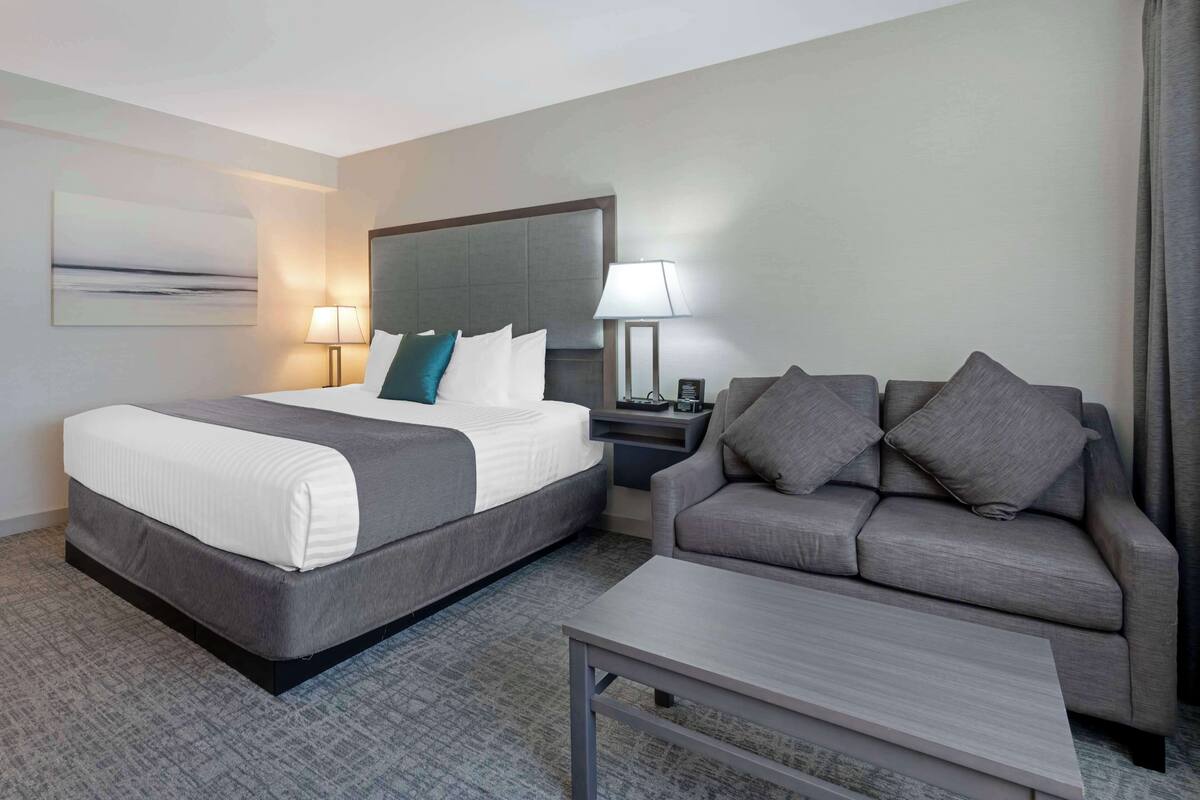 Una habitación de hotel con cama, sofá, mesa de centro y mesita de noche con lámpara.