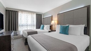 Een hotelkamer met twee bedden, een bureau, een televisie en een raam met gordijnen.