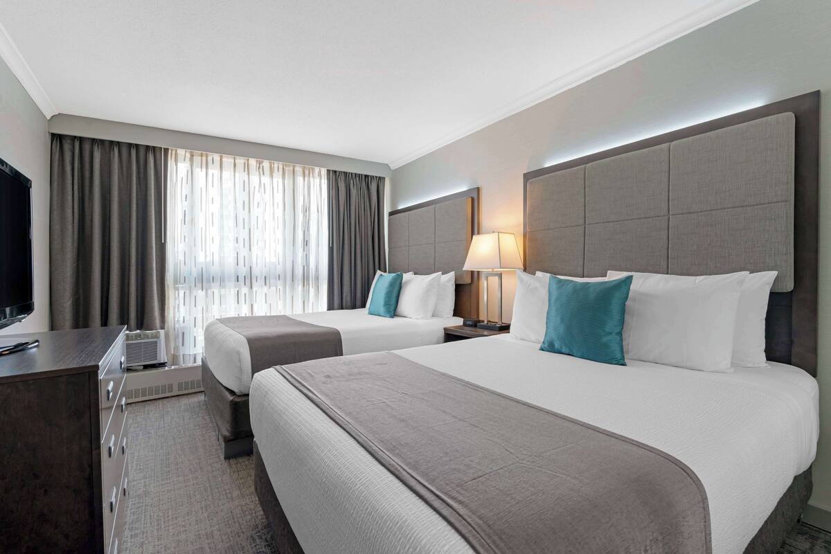Habitación de hotel con dos camas, un escritorio, un televisor y una ventana con cortinas.