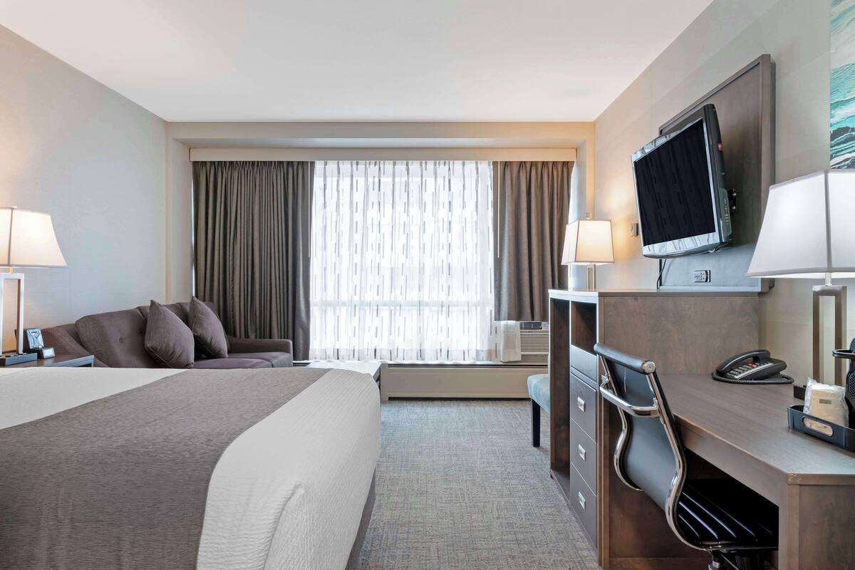 Habitación de hotel con cama, escritorio, silla, televisor y ventana con cortinas.